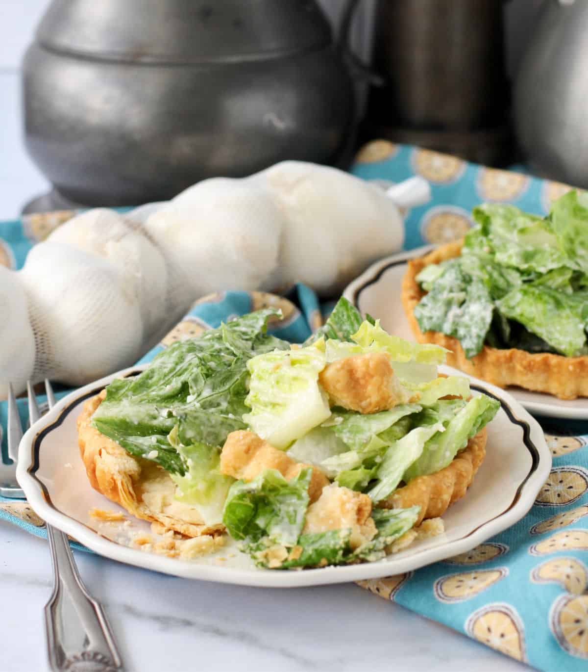 Caesar Tartlets with Sweet Garlic Butter Crusts on plates with whole garlic bulbs in background.