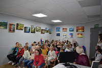 Zdjęcie przedstawia dzieci siedzące w czytelni biblioteki podczas spotkania.