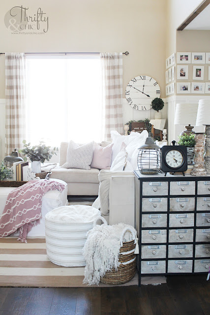 living room with white couch, large window, stacked wood, and shiplap mantel