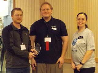 Jeff Peterson holding award, standing next to Ben Benson and Liz McMillan.