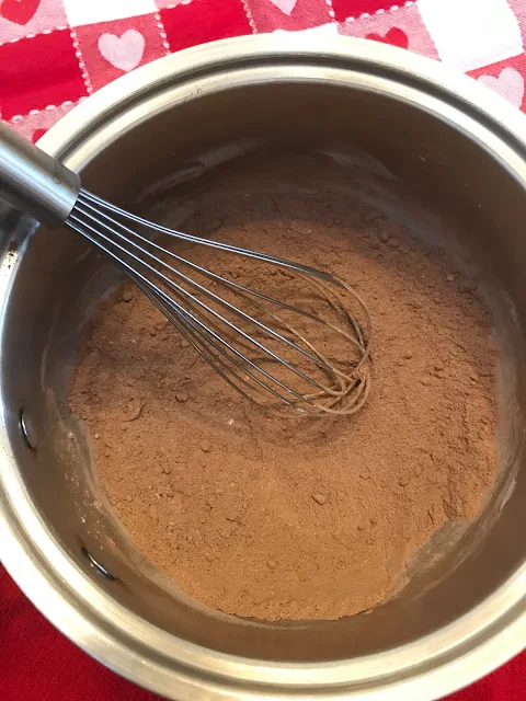 Pan with dry ingredients being whisked together for chocolate pudding.