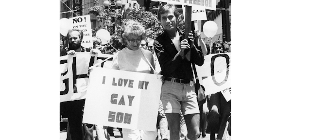 Woman marching with young man holding a sign reading "I love my gay son" SF pride parade circa 1977