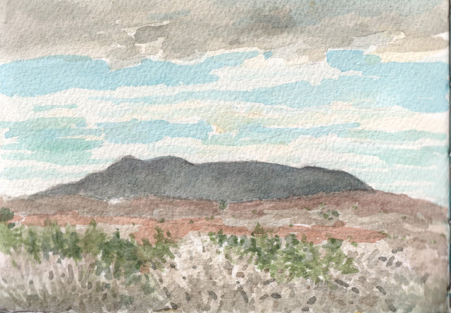 watercolor of distant mountain against partly cloudy sky, hills covered in bare trees and evergreens in foreground.