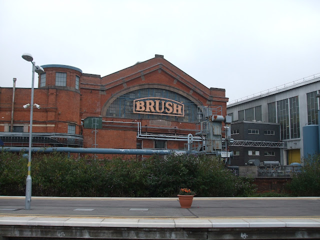 Industrial red brick building with neon sign and railway station platform in foreground