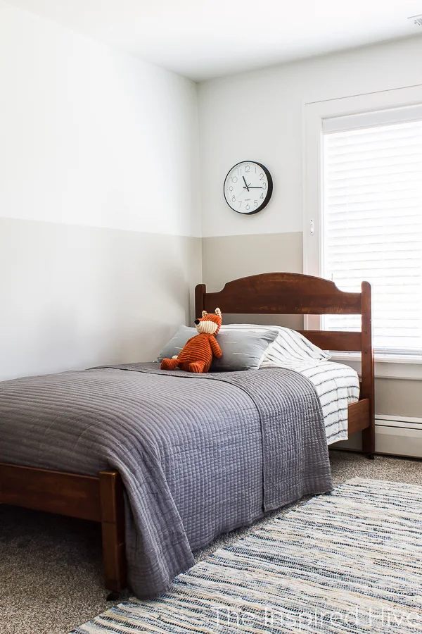 Boy's bedroom with antique bed, grey quilt, and blue pillow. 