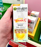 A white hand holding a white  Garnier Vitamin C Anti-Dark Spots & Brightening Serum in black font on a bright background
