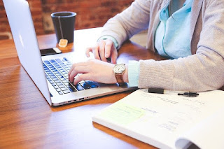 woman professional sitting at table and working on laptop computer with book and coffee beside her