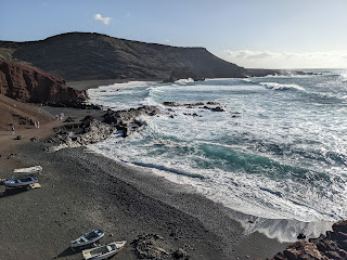 beach on Lanzarote with dark volcanic mountains and some small boats