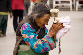 An elderly Tibetan women holding a prayer wheel on the Lhasa's pilgrimage circuit of Barkhor. The Barkhor, a quadrangle of streets that surrounds the Jokhang Temple, is both the spiritual heart of the holy city and the main commercial district for Tibetans – Luca Galuzzi - www.galuzzi.it (CC-by-SA-2.5)