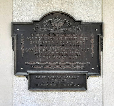 Bronze memorial plaque mounted to an exterior plain concrete wall