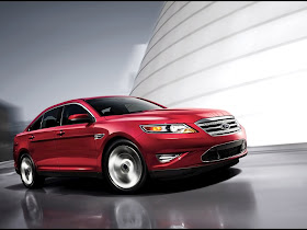 Front 3/4 view of red 2011 Ford Taurus driving around a building