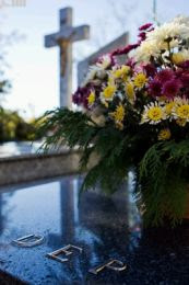 Fotografía de unas flores sobre una lápida en primer plano con la vista de una cruz al fondo