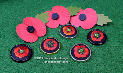 All five embroidered poppies shown with three paper remembrance poppies on green background