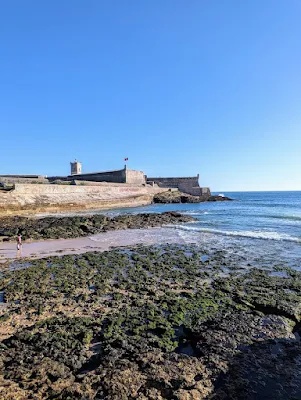 Forte de São Julião da Barra in the background with sand and surf in front at Carcavelos Beach near Lisbon. The top half of the picture is a bright blue Portuguese sky