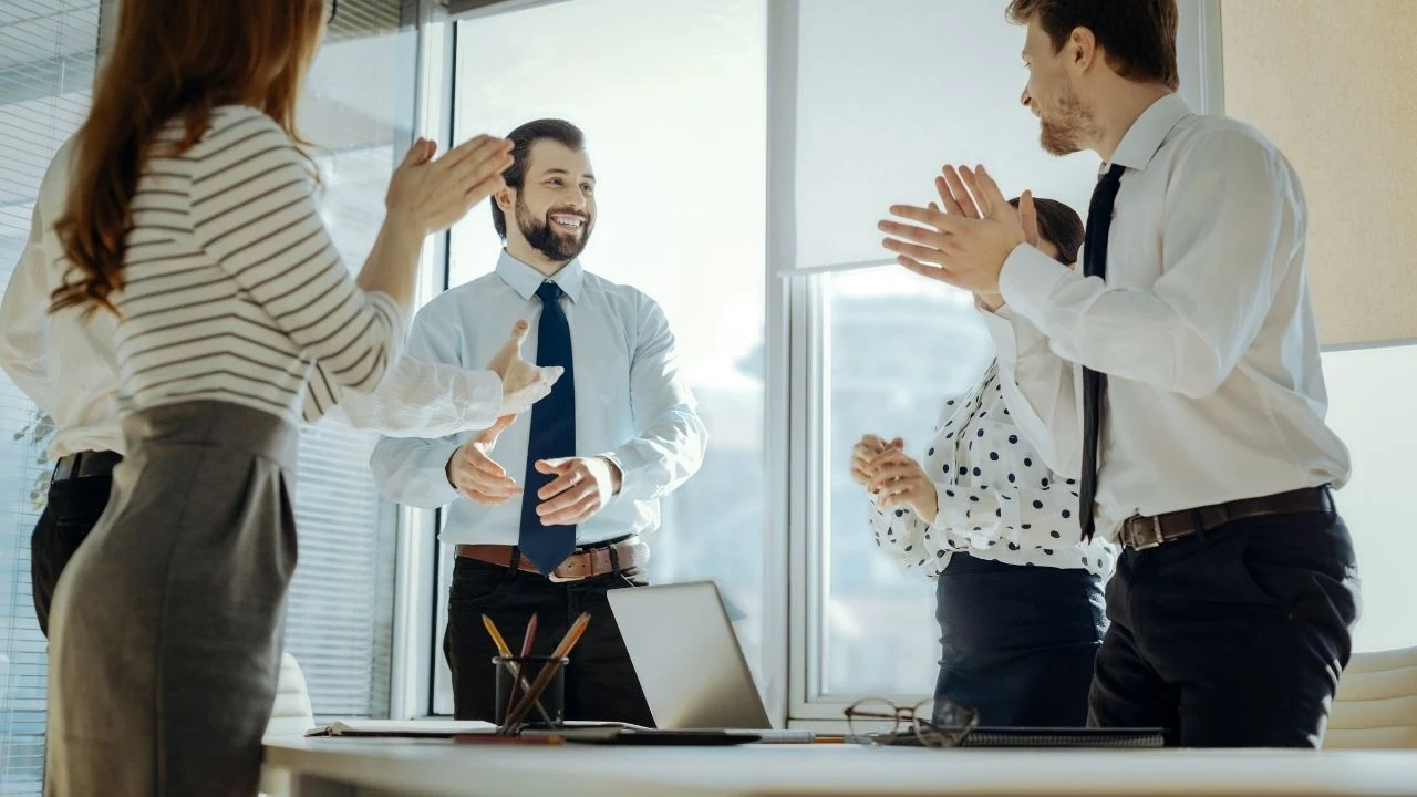 Joyful employees clapping their hands congratulating their colleague with promotion.