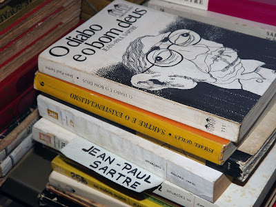 vários livros empilhados e um papel escrito Jean Paul Sartre