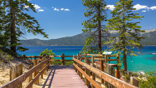 View from a hiking trail overlooking Lake Tahoe, with panoramic vistas of the lake surrounded by mountainous terrain.