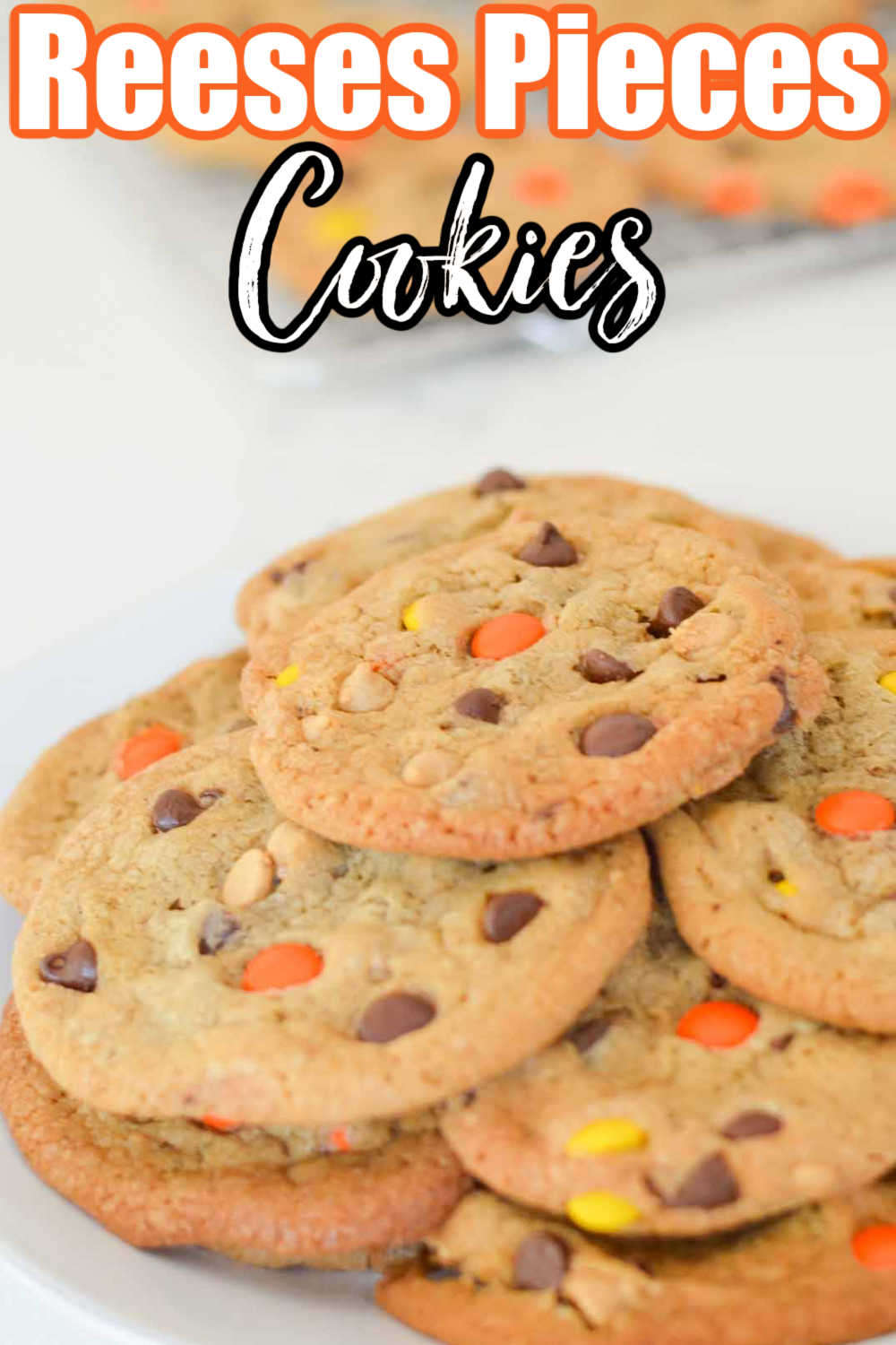 A side shot of a stack of Reeses Pieces Peanut Butter Chip Chocolate Chip Cookies on a white plate.