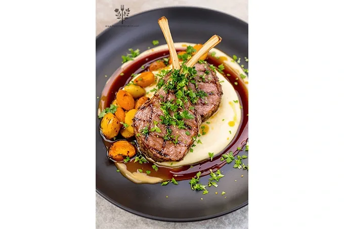 Rack of Lamb with Mint Gremolata plated with tender lamb chops, creamy parsnip purée, roasted vegetables, red wine reduction, and vibrant mint gremolata.