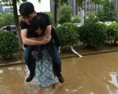 Chinese woman pictured carrying her boyfriend on her back while crossing a flooded street so 'he won't ruin his expensive leather shoes' 