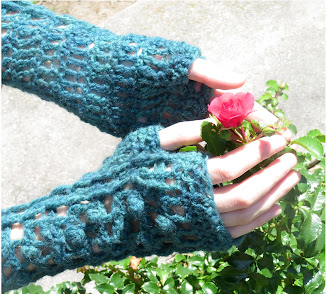 A person wearing a pair of fingerless crochet mittens.  They have their hands around a small flower.