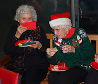 Two women in Christmas sweaters enjoying refreshments and chatting