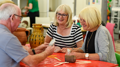 An adult pottery workshop - 3 adults are sat around a table, engaging in the crafts and discussing them with one another