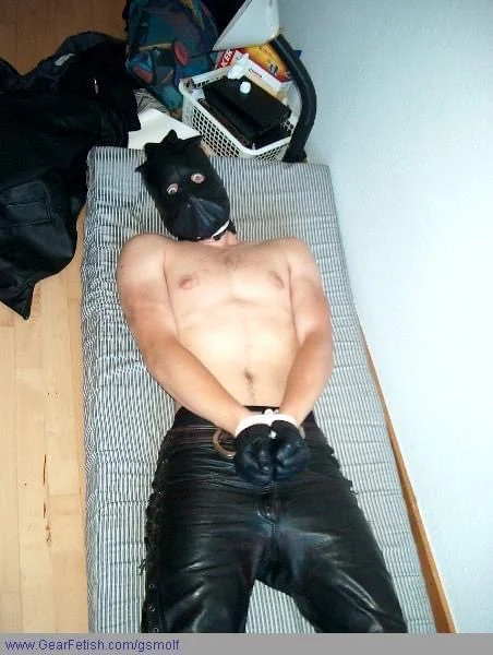 Black leather Hood with eye holes on naked man handcuffed laying on bed