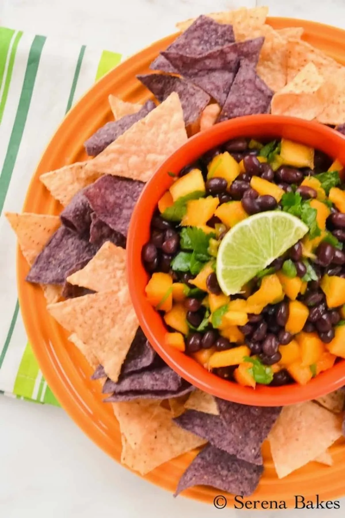 A down shot of Mango Black Bean Salsa in a orange bowl with chips around the edge.