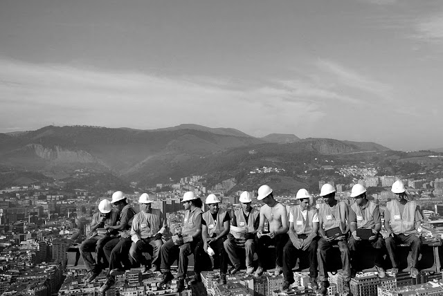 Black and white photo of workers on the skyscraper with the city skyline in the background