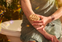 A wide angled photo of someone using  an oval ridged massage bar with magik engraved on the top that’s in purple and green on a bright background