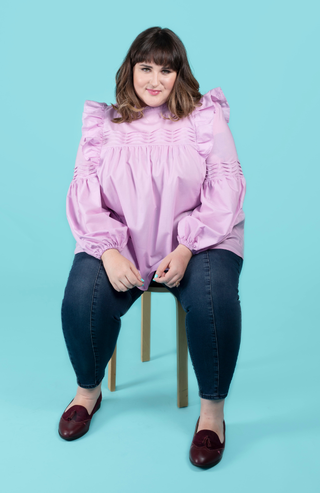 Model sitting down wearing a lilac blouse with tuck details, made using the Marnie sewing pattern in cotton lawn.