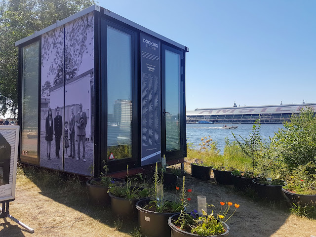 Image of The Docking Station the Smallest Work Space in Amsterdam. It looks like a small glass box, almost like a shed and it overlooks the canal and centraal station is situated on the opposite side of the canal.