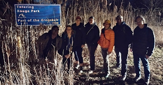 Seven people in a grass field at night standing by a sign that says "Entering Rouge Park"