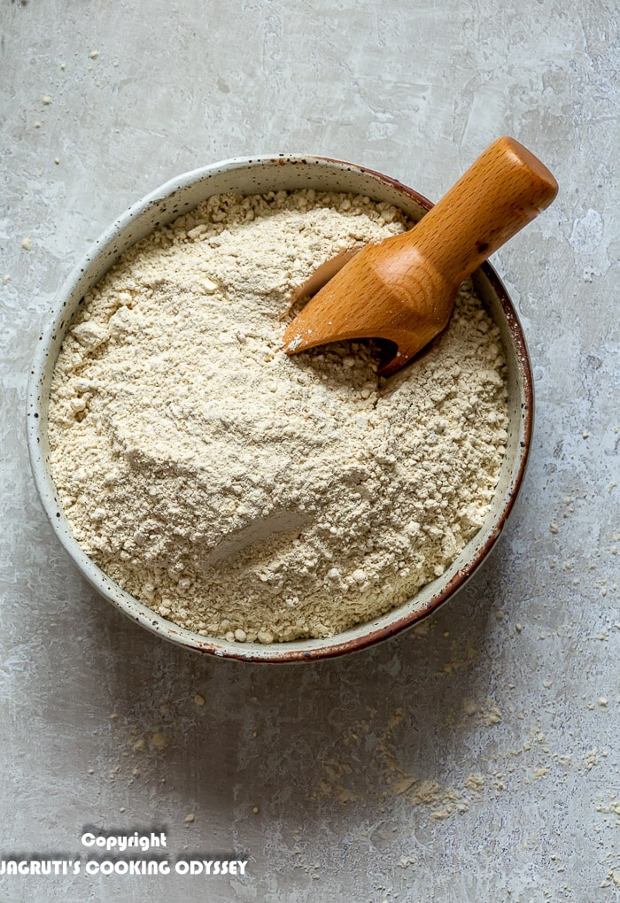 Mixed multigrain flour for roti/chapatti is in a beige bowl with a wooden scoop