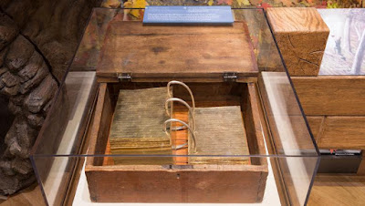 A wooden chest with what could be pages in a pocket-sized loose-leaf binder, except the pages are golden plates.