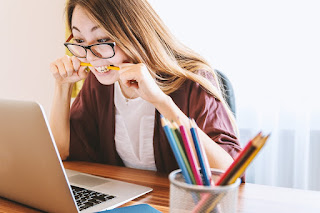 A young woman at a laptop bites into a pencil