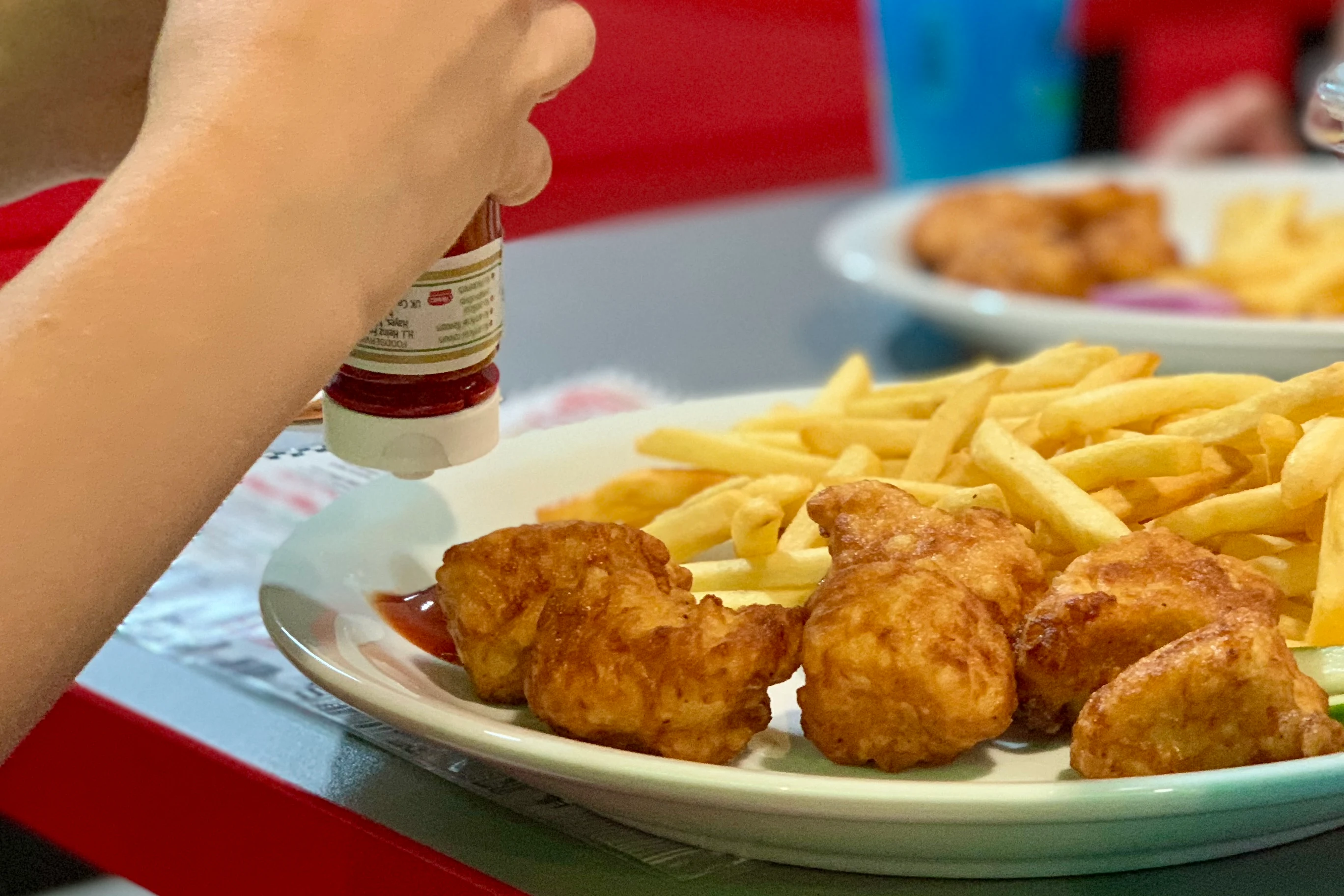 a child squeezing tomato ketchup onto a plate with chicken nuggets and chips