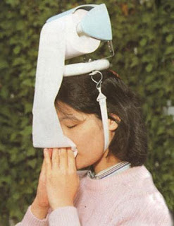woman with toilet roll holder attached to her head blowing her nose with toilet roll from it
