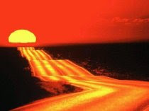 Fotografía en la que se muestra una amplia carretera que atraviesa el desierto en dirección al sol que se pone en el horizonte