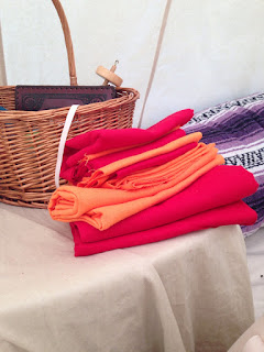 A stack of screaming red and bright-orange pieces of fabric, folded and set on a tan-covered table next to a basket inside a canvas tent.