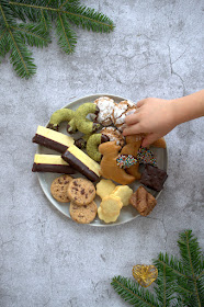 Keksteller mit sieben weihnachtlichen Sorten – eine Kinderhand greift nach einem Keks.