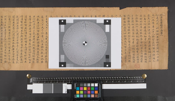 Black background behind a yellowed scroll with Chinese characters on it and a black and white focus target with a multicoloured colour palette and black and white strips at bottom of image.