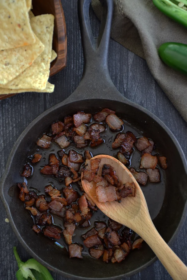 Crispy diced bacon cooked to perfection in a cast iron skillet, emitting a mouthwatering aroma.