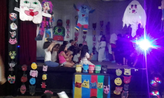 la imagen muestra varios alumnos en el escenario del salon de actos representando una canción