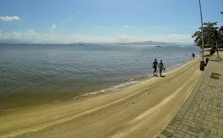 Una pareja camina despreocupada sobre la tranquila playa de arena gruesa y firme de Cacupé Grande. El mar llega a la costa si  hacer ningun tipo de ola. Parece un lago mas que un mar.