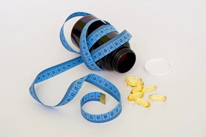 A measuring tape around a weight loss diet pill bottle with gelly like pills lying on a white background