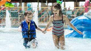 Image of children running in a shallow pool one child in life preserver