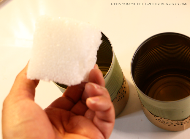 Hand holding foam block over two metal cans