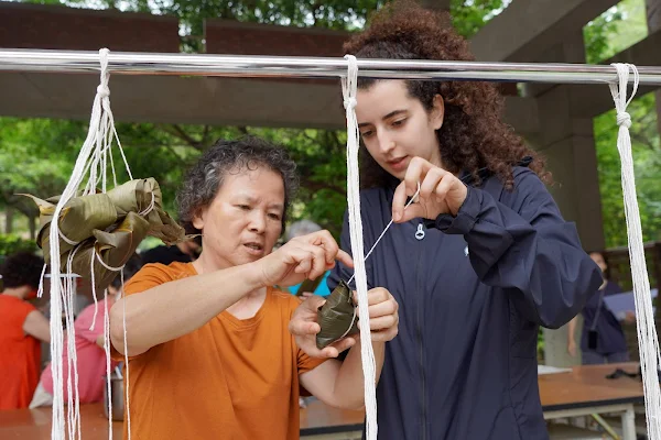 ▲大葉大學法國學生蘇莉娜(右)在長青大學阿媽的教學下綁粽子。（大葉大學提供）